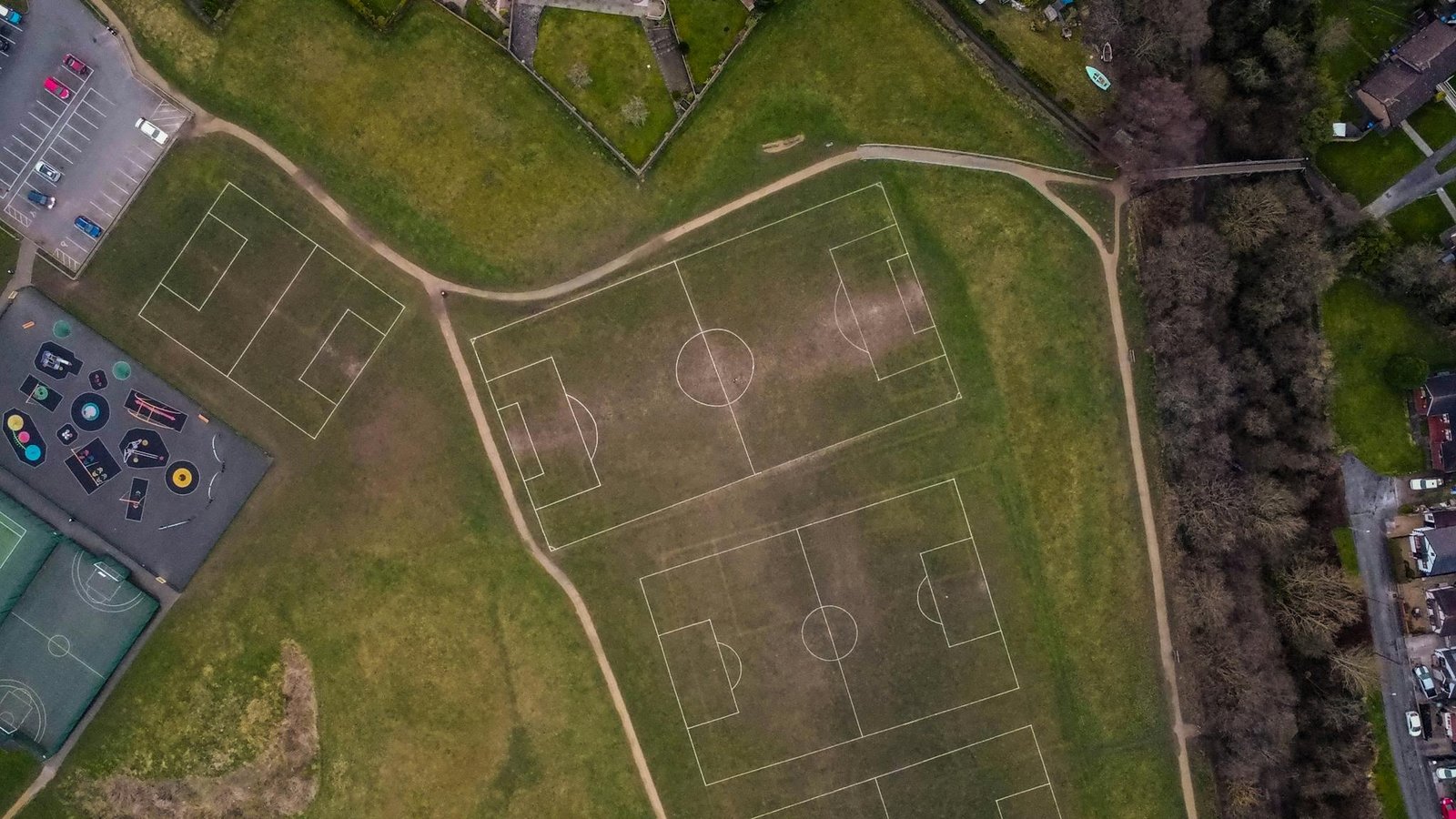 Drone shot of soccer fields and basketball courts in a green urban park area.