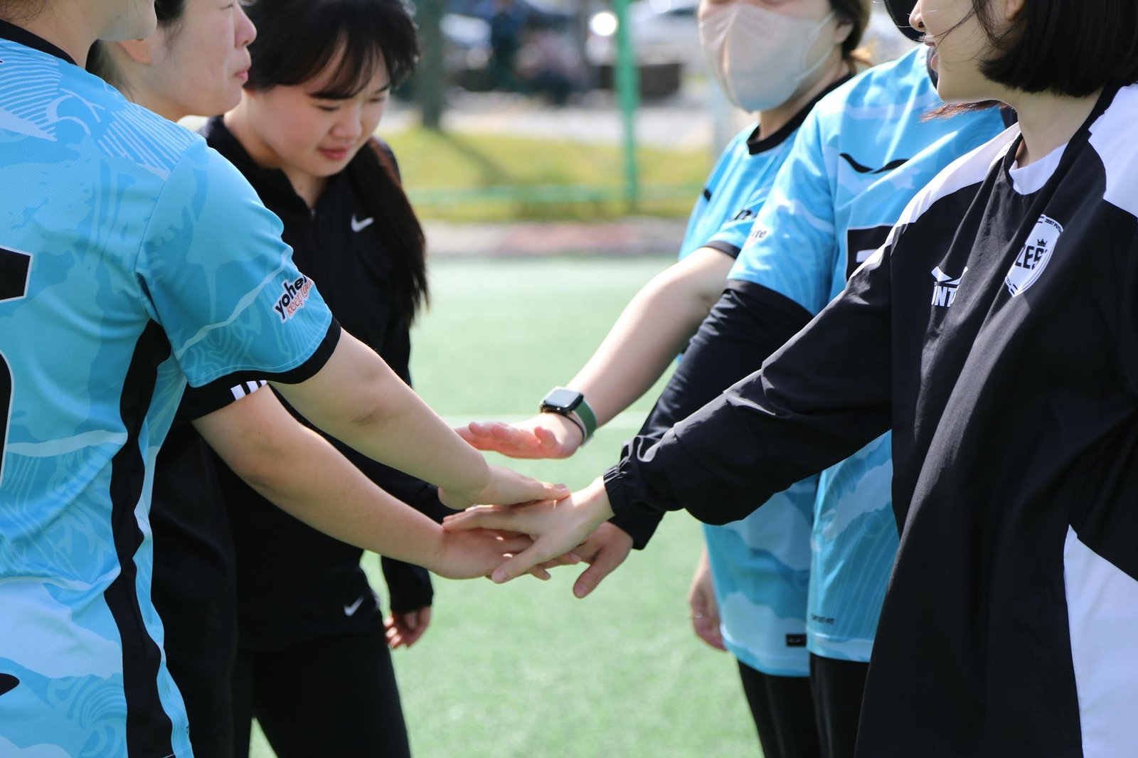 Women football players unite in a triumphant team gesture outdoors.