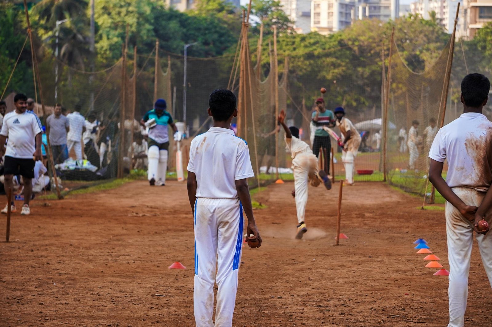 Young cricketers practice their skills on a dusty pitch in a Mumbai playground, showcasing local sports culture.